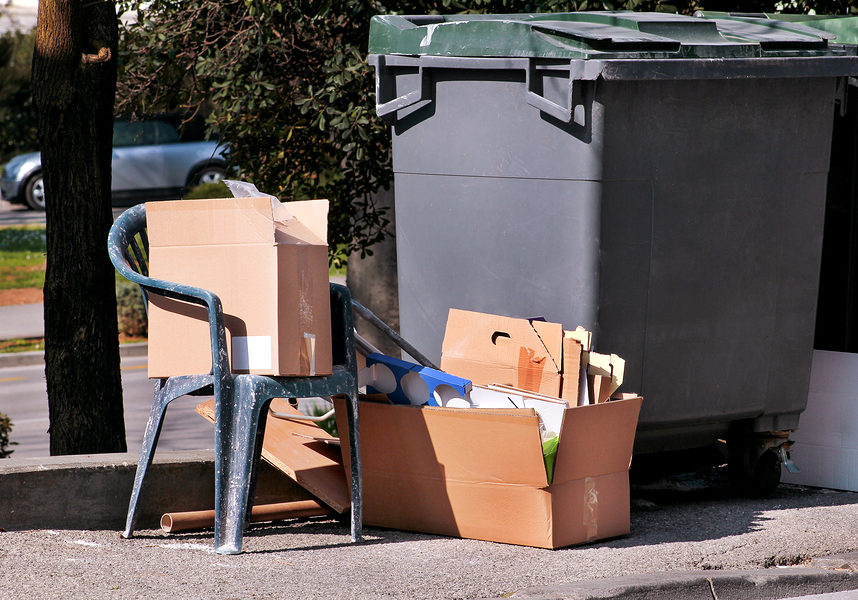 Waste left next to trash dumpster on the street. Cardboard boxes and old plastic chair near the container, trash dumpsters. Dirty refuse bins. Street scene. Recycling industry. Ecology. Not Ecology.