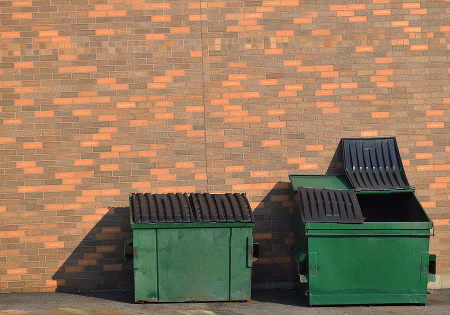 Green recycling dumpsters against a brick wall